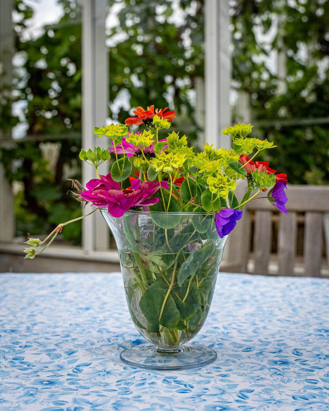 Farverig buket med zinnia, lathyrus og grønt i glasvase Farverig buket med zinnia, lathyrus og grønt i glasvase